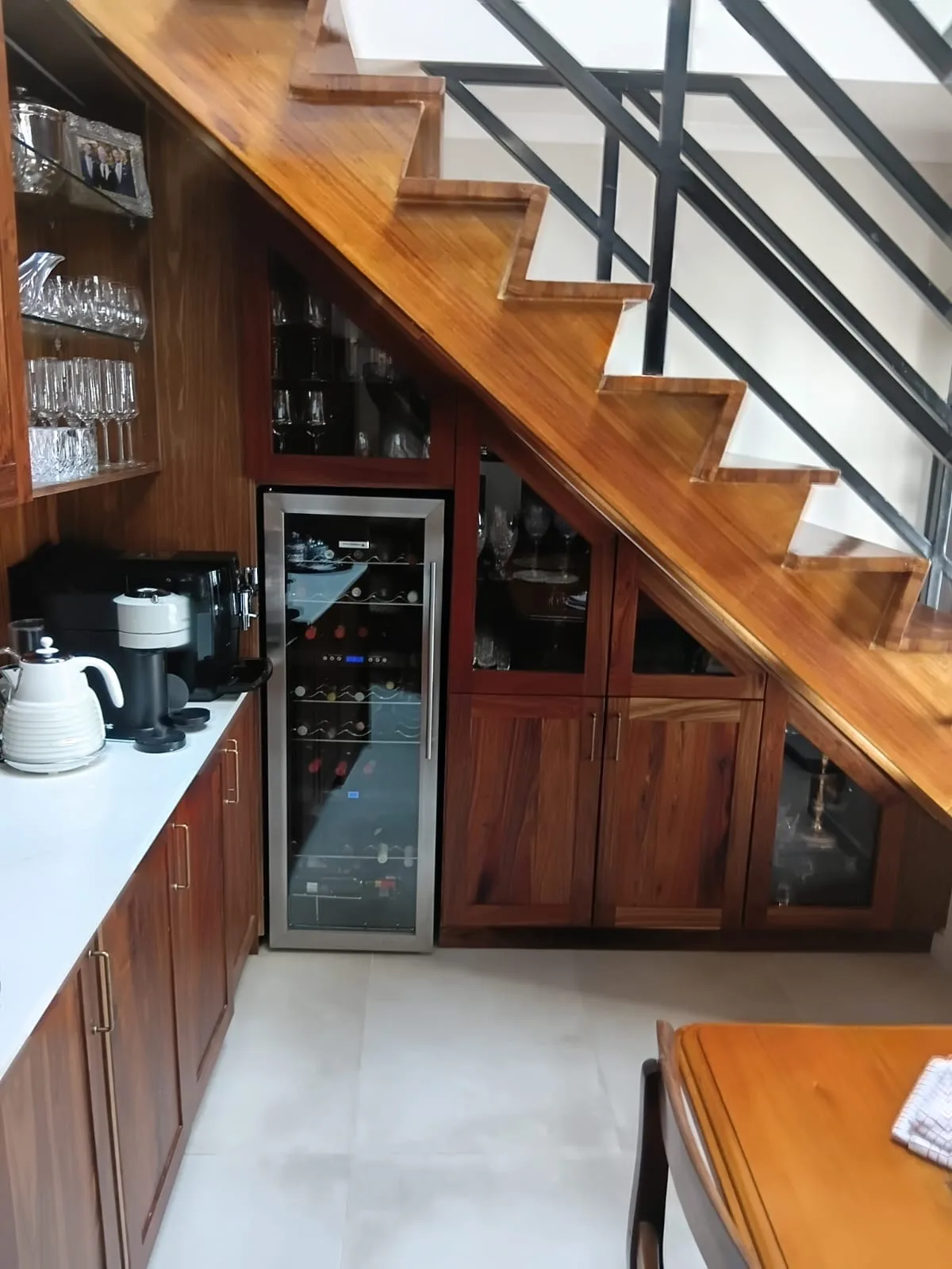 Wine Fridge and Display Cabinets — Close in on the wine fridge and the glazed cabinets beside it, each one cut to follow the angle of the stair above so nothing is boxed in and nothing is wasted.
