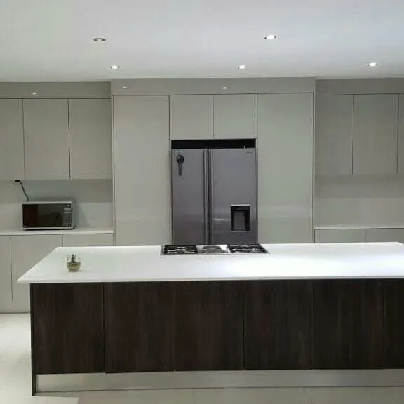 A handleless kitchen in soft white, wrapped floor-to-ceiling around an integrated fridge, with a white quartz island top over a dark oak base — built and installed in Sandton