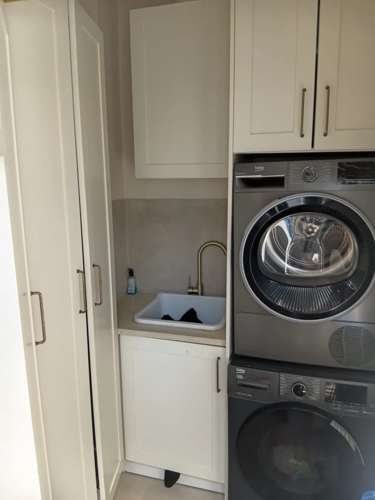 Laundry Tall Units — The other side of the same laundry: a pair of full-height shaker cupboards for brooms, ironing board and linen, squared into the corner beside the machine housing.