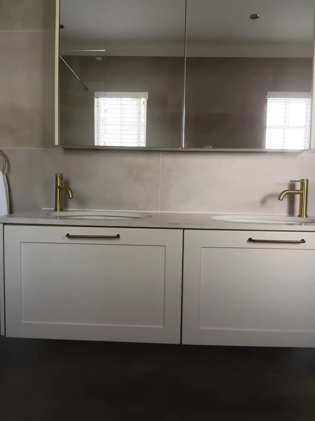 Floating Vanity with Mirror Cabinets — A wall-hung vanity with two deep shaker drawers and brass handles, floating clear of a dark tiled floor, with a run of mirrored cabinets above for storage that doesn't show.